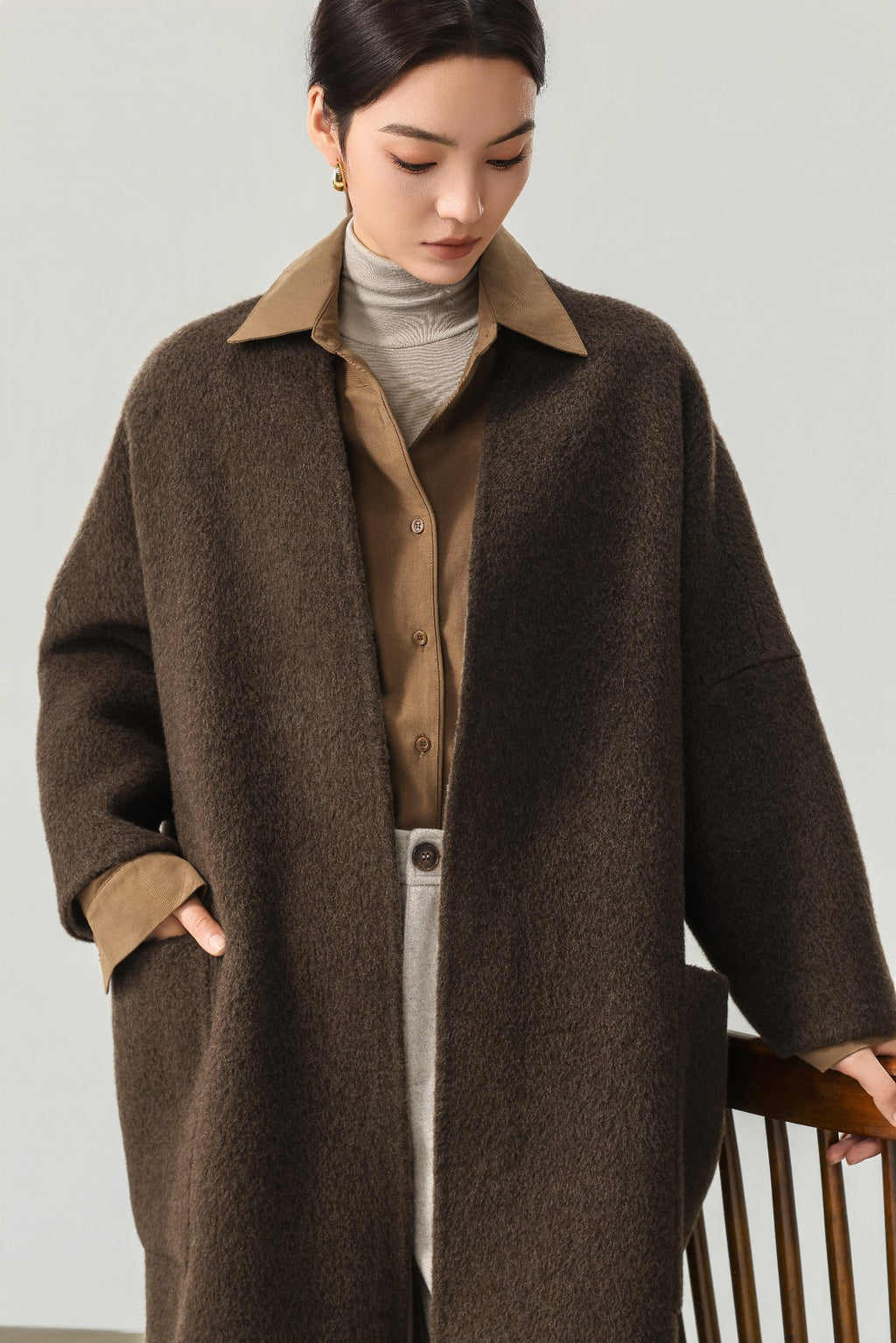 Close view of the dark brown coat showing the neckline, dropped shoulder and patch pocket; the shirt is styling only.