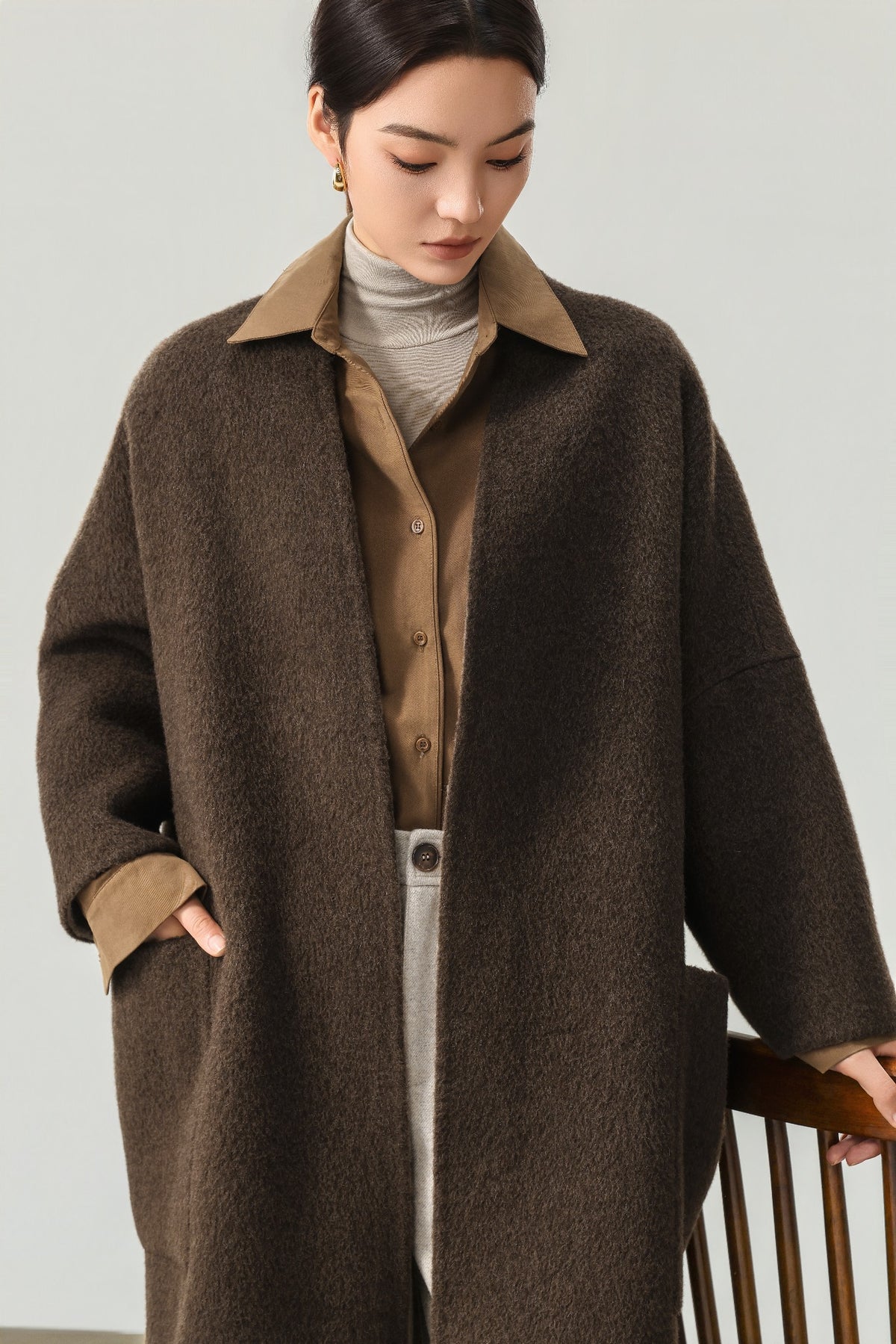 Close view of the dark brown coat showing the neckline, dropped shoulder and patch pocket; the shirt is styling only.