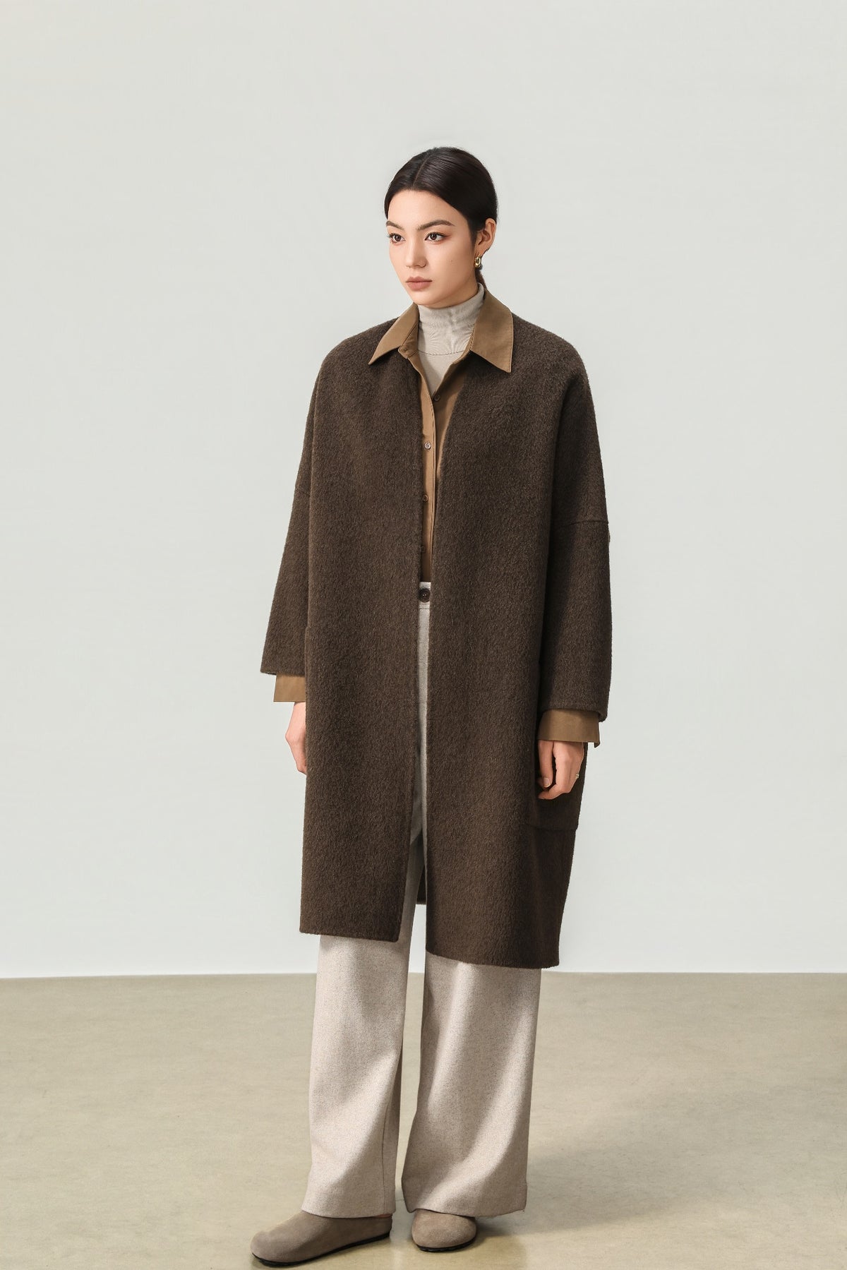 Dark brown wool and yak-blend collarless coat worn over a brown shirt and cream trousers.