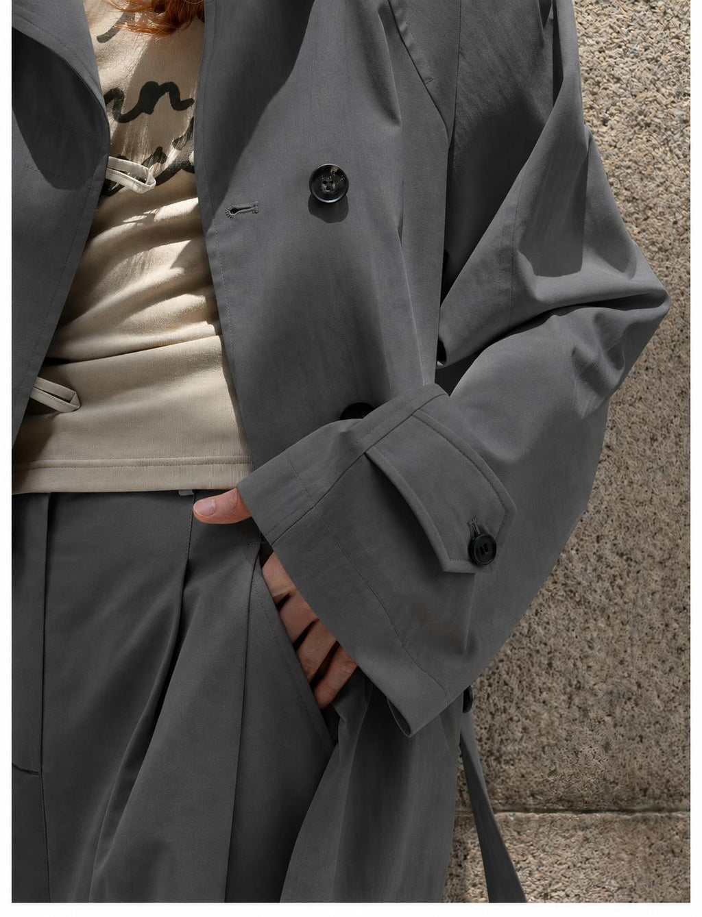 Close-up of the Dark Grey trench coat's front buttons, side pocket and buttoned cuff tab.