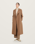 Brown coat with leather collar detail, worn with a cream roll-neck and taupe trousers.