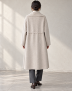 Vienna coat in Oats, relaxed rear model view with centre back seam and integral drawcord channel — AI-assisted styling image.